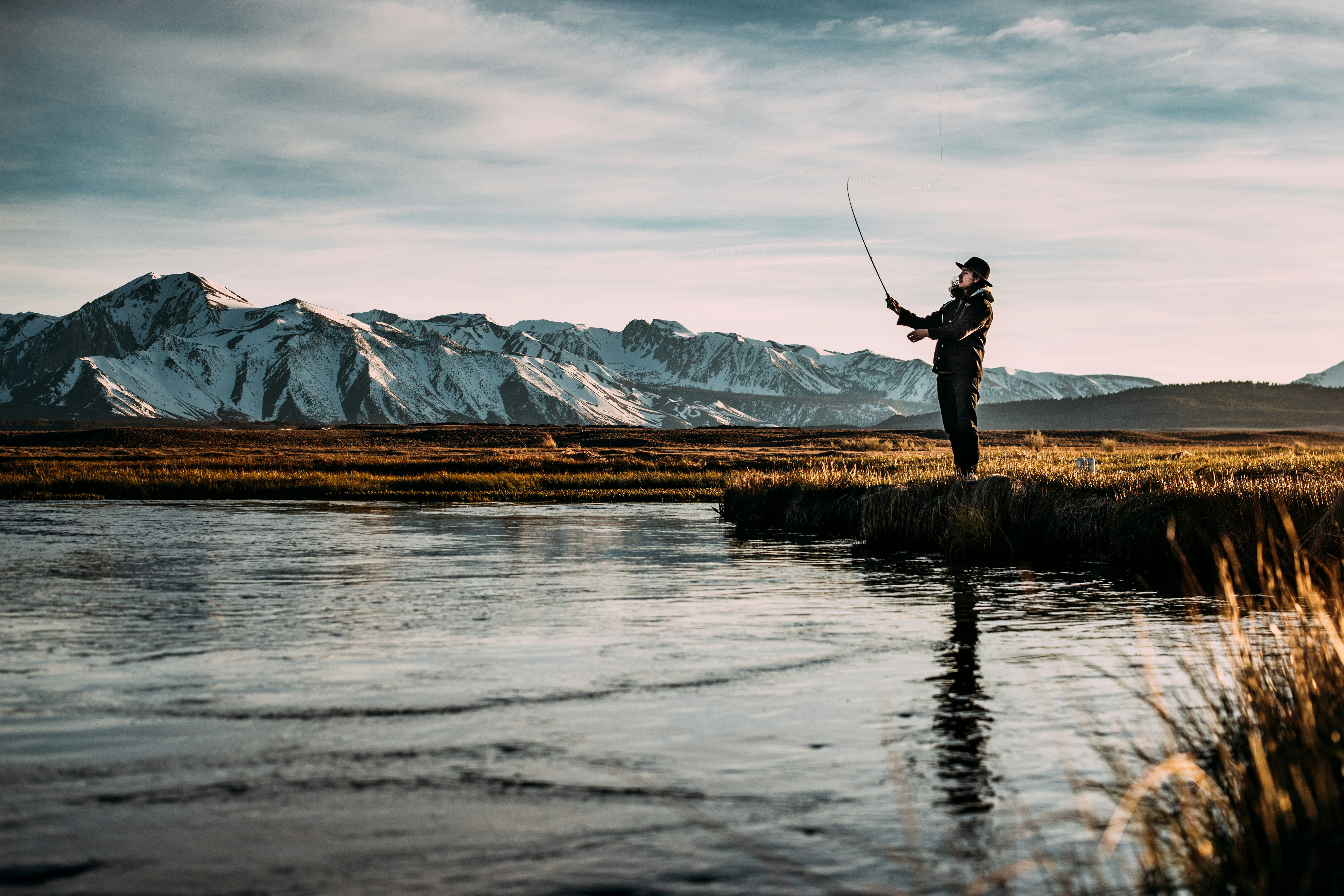 landscape photo of man fishing on river near mountain alps